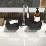 A black silicone faucet splash guard with a bar of soap and a pump bottle on a white kitchen sink, with a window and wooden