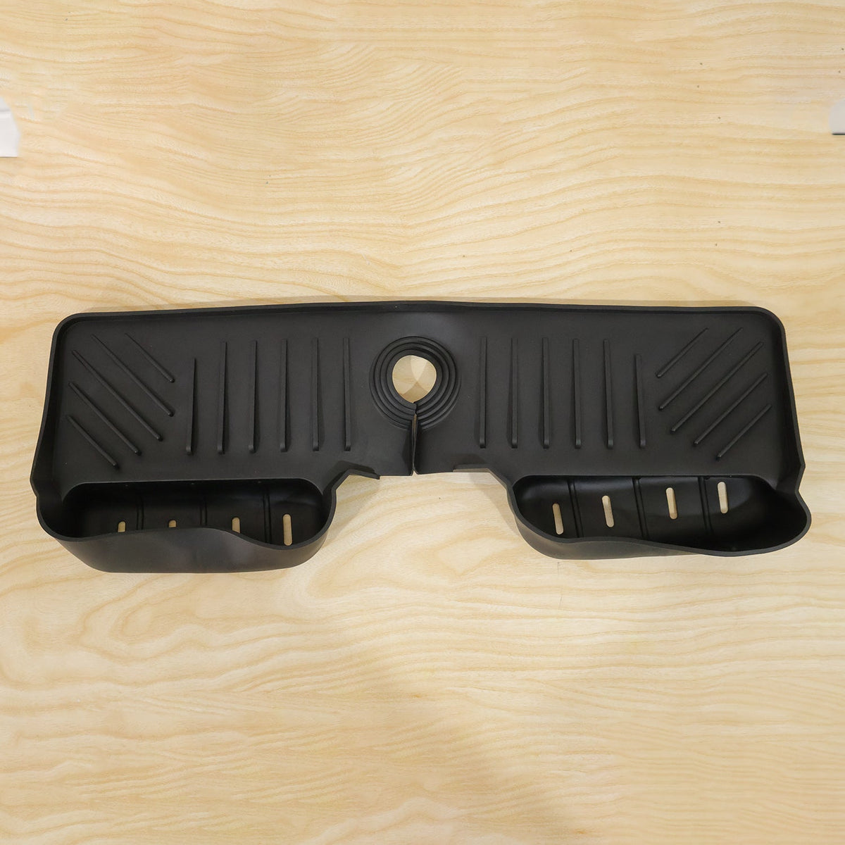 A black silicone faucet splash guard with drainage grooves and two side compartments, lying flat on a light wood surface.