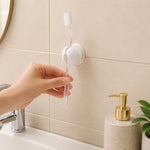 A hand placing a clear toothbrush into a white wall-mounted holder above a sink with a gold soap dispenser.