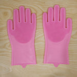 A pair of pink silicone scrubbing gloves with textured palms laid flat on a light wooden surface.