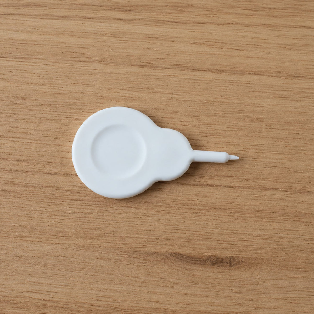 A small white plastic tool with a circular base and a pointed end rests on a light brown wooden surface.