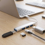 A silver Type C to four-port USB hub connected to a laptop, with various adapters and a USB drive on a wooden desk.