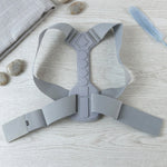 The gray posture corrector laid flat on a light wooden surface with decorative stones and a blue feather.