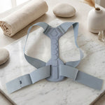 The gray posture corrector laid flat on a white marble surface with rolled fabric and decorative items.