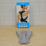The gray posture corrector laid flat on a wooden surface in front of its blue and white product box.