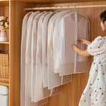 A woman zips up a translucent garment bag with a white zipper in a wooden wardrobe filled with other bags.