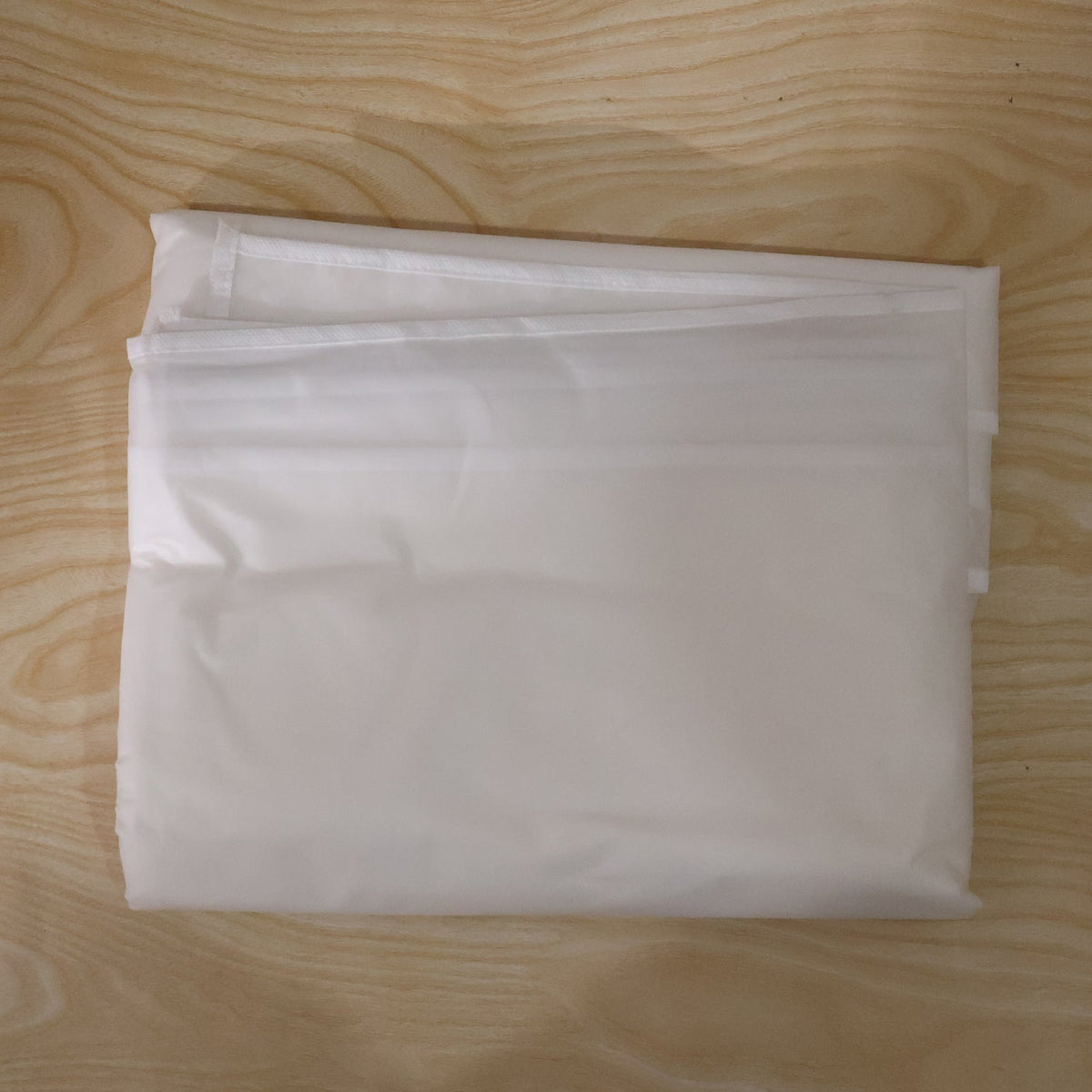 A translucent garment bag is folded neatly on a light wood surface.