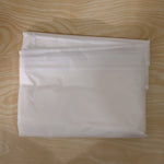 A translucent garment bag is folded neatly on a light wood surface.