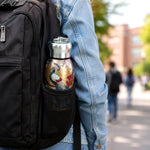 Golden stainless steel vacuum bottle with a peacock print tucked into the mesh pocket of a black backpack.