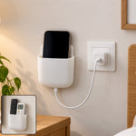 White adhesive organizer holding a black smartphone, charging from a wall outlet beside a wooden nightstand.