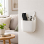 White adhesive organizer mounted on a wall, holding a black remote, glasses, and a silver pen.
