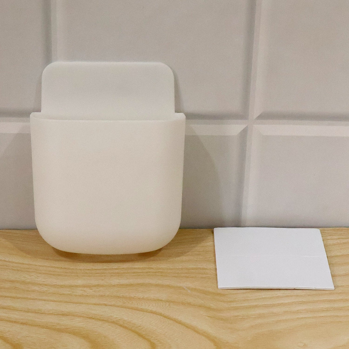 White adhesive organizer on a wooden surface next to a white adhesive pad, against a tiled wall.