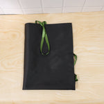 A black apron with green ties is folded neatly on a light wooden surface.