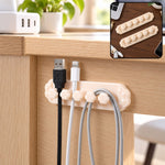 Beige flower-shaped cable organizer clip with five slots holding black, white, and grey cables under a wooden desk.