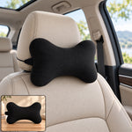 Black microbead bone-shaped pillow attached to a tan car seat headrest with a small inset showing it on a wooden surface.