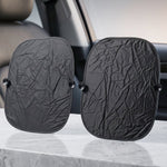 Two black foldable car sunshades with suction cups are displayed upright on a light-colored surface inside a car.