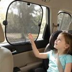 A young girl in a car seat reaches towards a black mesh foldable sunshade with suction cups on the car window.
