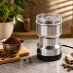 A stainless steel electric grinder sits next to a bowl of ground coffee and whole coffee beans on a wooden board.