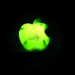 A glowing green apple-shaped LED night light plugged into a dark wall socket.