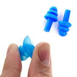 A person's fingers hold a blue silicone earplug, demonstrating its flexibility, with two more earplugs in the background.