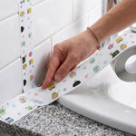 A hand pressing white cartoon-printed sealing tape into the corner of a bathroom sink and tiled wall.