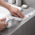 Hands applying white cartoon-printed sealing tape around a bathroom sink edge, with a small inset showing the tape – view 7