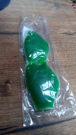A green gel eye mask is sealed in clear plastic packaging, resting on a wooden surface.