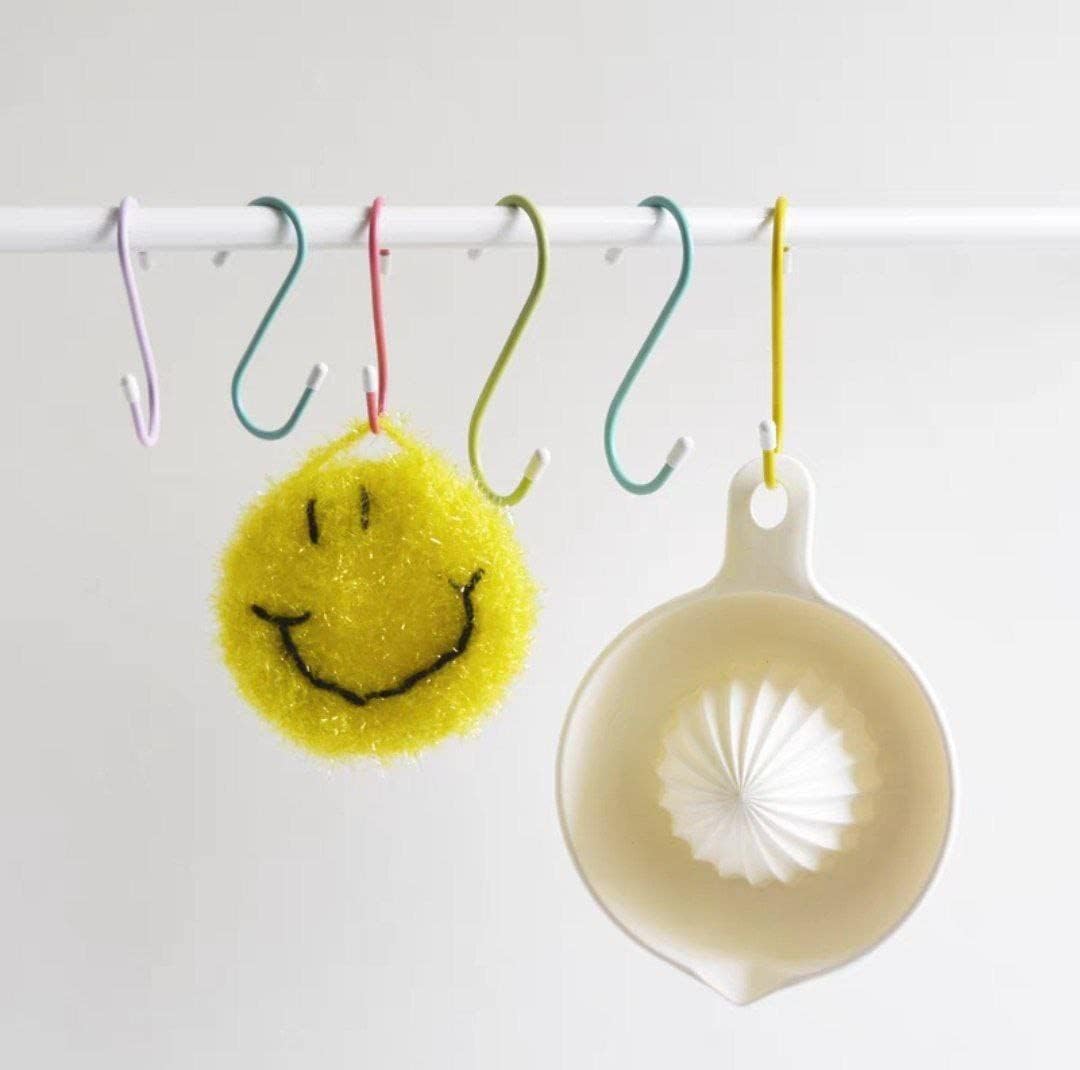 Four colorful plastic coated S hooks hanging a yellow smiley face sponge and a white citrus reamer.