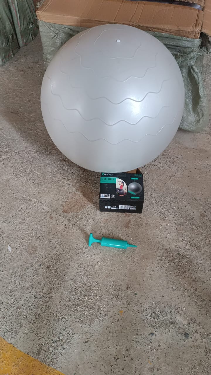A large grey stability ball with a wavy texture sits on a concrete floor next to a small black box and a teal air pump.