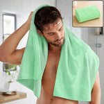 A man drying his hair with a light green microfiber towel in a bathroom, with a folded towel inset.