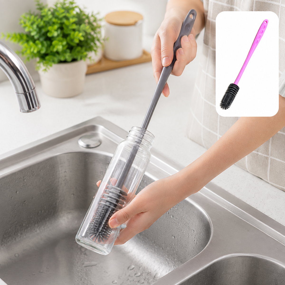 A person cleaning a clear glass bottle with a grey silicone brush in a kitchen sink.
