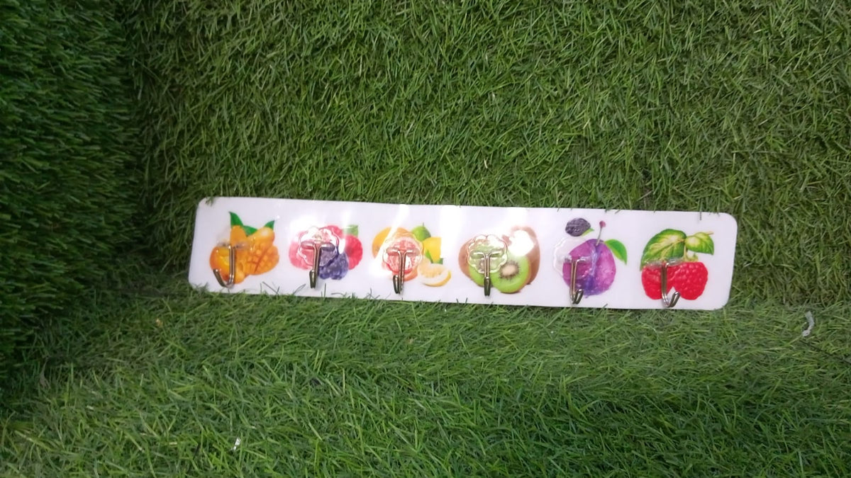 A white adhesive wall hook strip with fruit designs is placed on a vibrant green artificial grass surface.