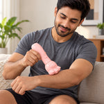A man in a grey t-shirt uses a pink bear paw shaped massager on his upper arm while sitting on a couch.