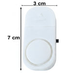 A white plastic magnetic door alarm is shown with its dimensions, 7 cm in length and 3 cm in width, indicated by arrows.