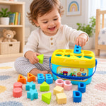 A smiling baby plays with a blue and yellow shape sorter bucket and colorful alphabet and geometric blocks on a patterned