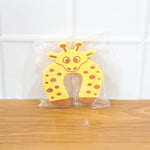 A yellow giraffe-shaped EVA door stopper is sealed in clear plastic packaging, resting on a wooden floor.