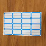 A sheet of blue-bordered rectangular label stickers with blank white centers is displayed on a wooden surface.
