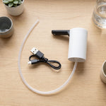 The white and black electric water dispenser pump with its clear silicone tube and black USB charging cable laid out on a