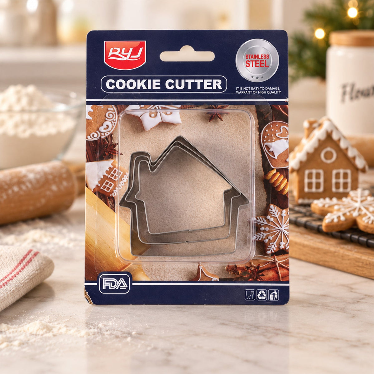 Three stainless steel house-shaped cookie cutters in clear packaging, surrounded by baked gingerbread cookies and baking