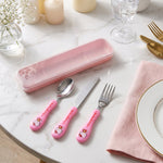 Pink Hello Kitty spoon, knife, and fork next to a pink case on a marble table.