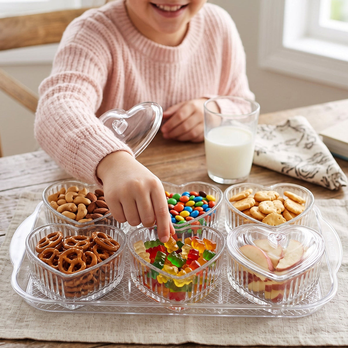 A top-down view shows six empty, clear, ribbed heart-shaped bowls with lids on a transparent serving tray on a wooden