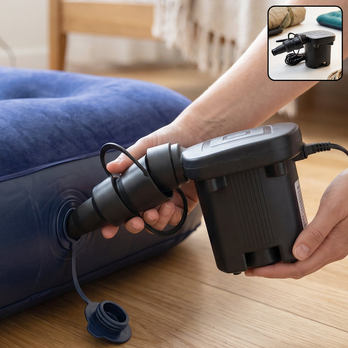 A person's hands are using a black electric air pump to inflate a dark blue inflatable mattress on a wooden floor.