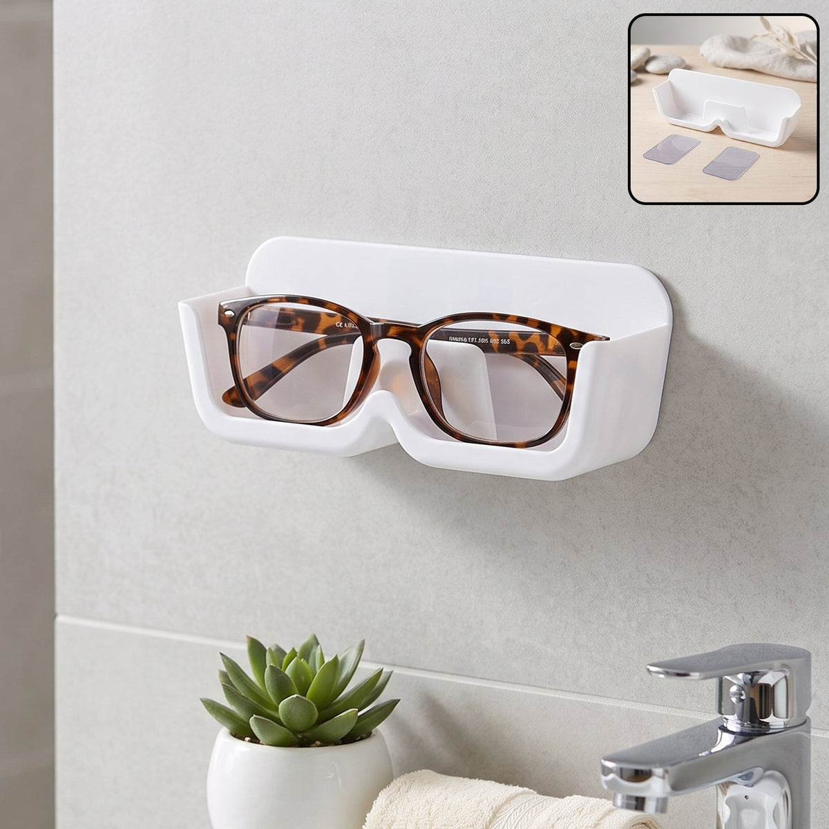 White plastic wall-mounted eyewear holder with tortoise-shell glasses, above a sink with a small green plant