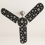 A ceiling fan with black and white floral dust covers on its blades and motor, viewed from below.