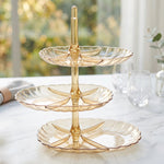 An empty three-tier amber acrylic dessert stand with scalloped edges rests on a white marble counter.