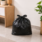 A full, tied black plastic garbage bag rests on a light gray tiled floor in an indoor setting.