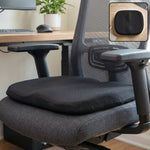 Black ergonomic memory foam seat cushion on a grey office chair with a small inset of the cushion on a wooden desk.