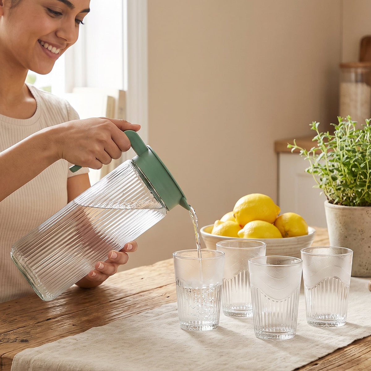 A clear, ribbed glass pitcher with a green lid and four matching tumblers are arranged on a plain white background.