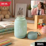 A mint green glass bottle with a bunny print sits on a desk, with a matching lid beside it. The bottle is labeled 380 ML and