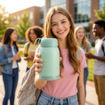 A smiling girl holds up a mint green glass bottle with a bunny print, with other students in the background.